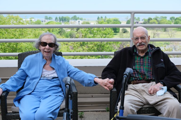 two residents seated and holding hands